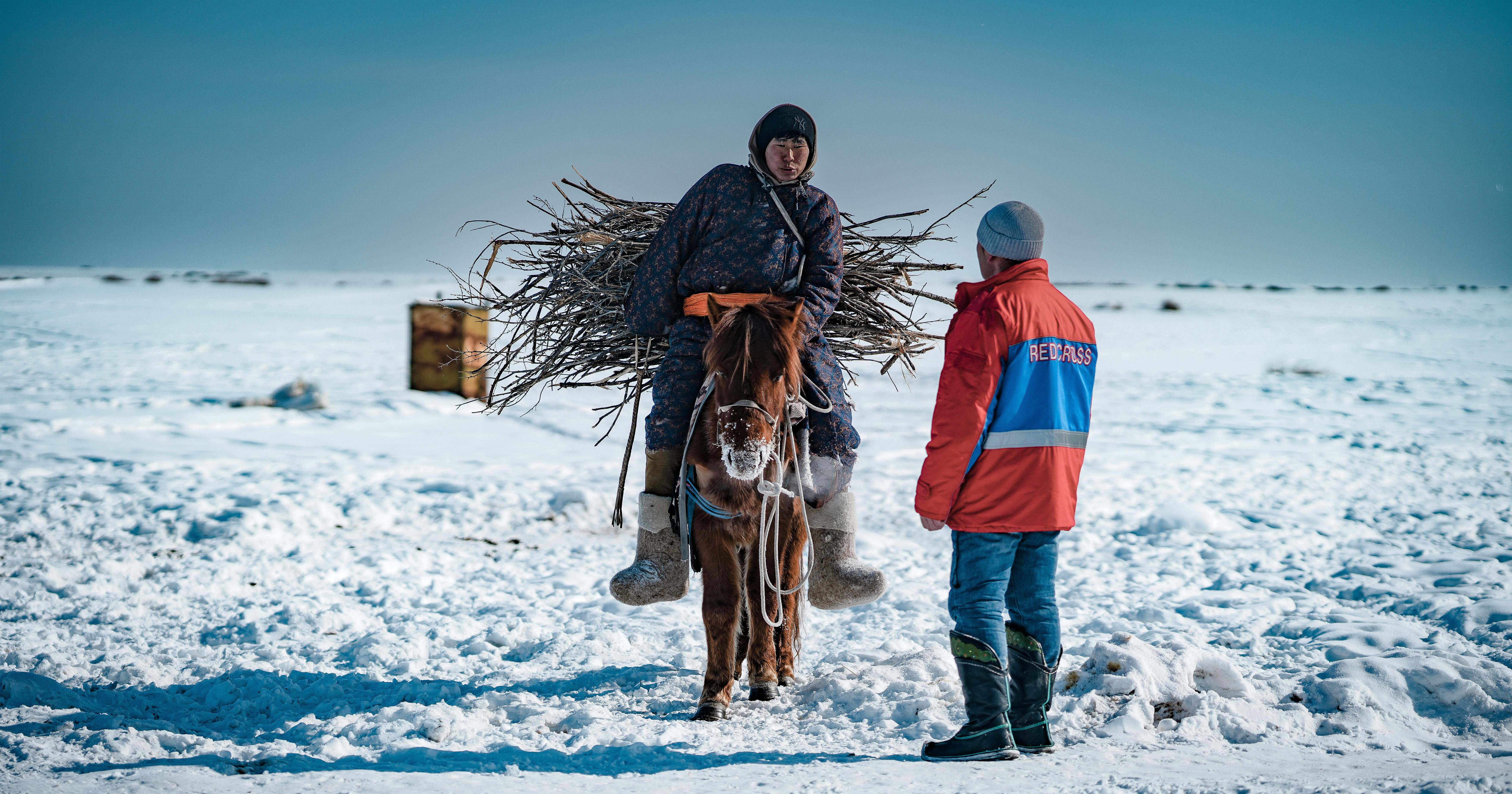 Punaisen Ristin vapaaehtoinen ja hevosella ratsastava mongolialainen henkilö keskustelemassa talvisessa maisemassa.