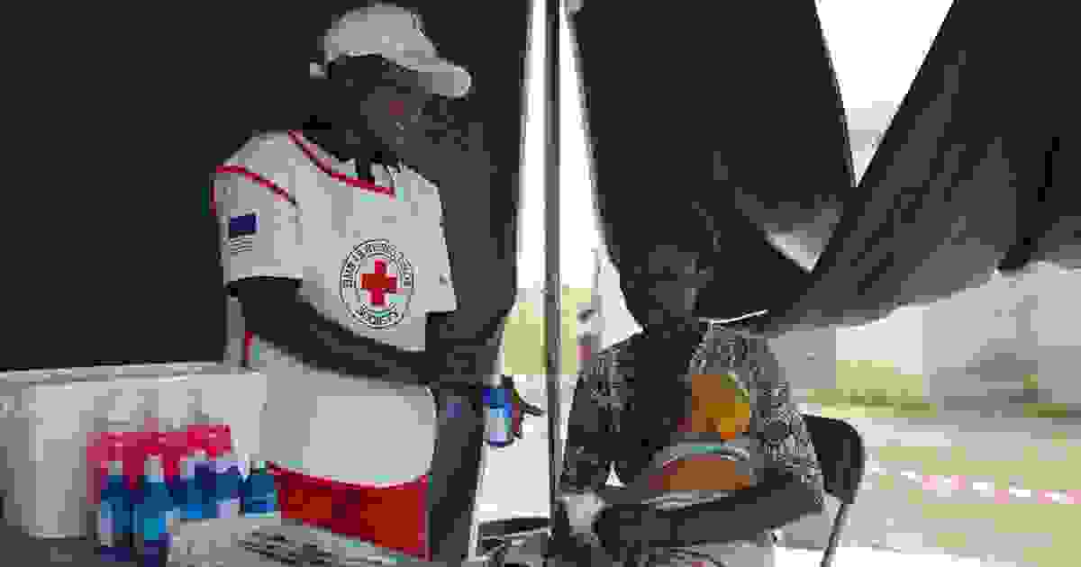 Punaisen Ristin vapaaehtoinen ojentaa vesipulloa tuolilla istuvalle henkilölle ja lapselle.