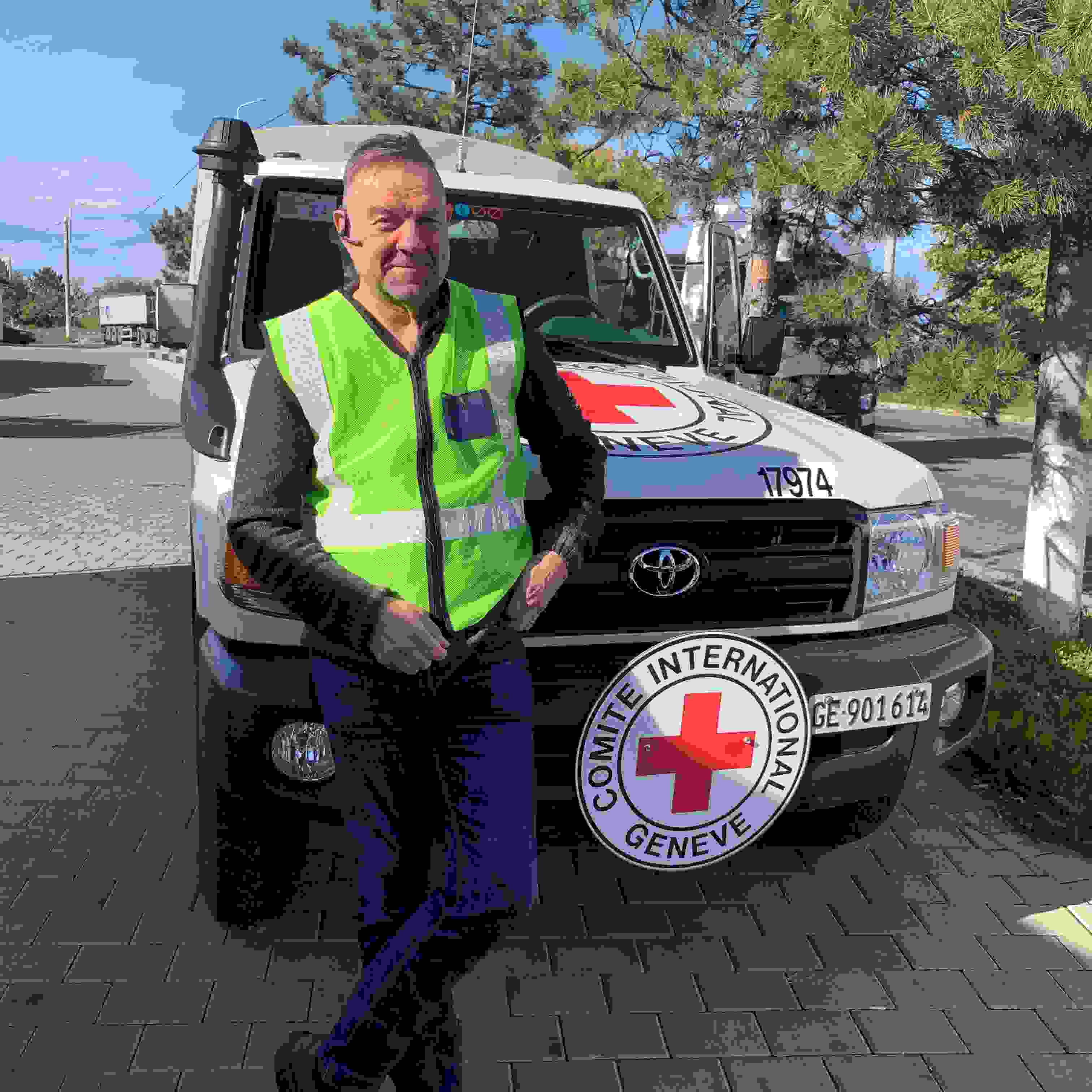 Avustustyöntekijä Keijo Eklöf seisoo hymyillen Punaisen Ristin kansainvälisen komitean auton edessä.