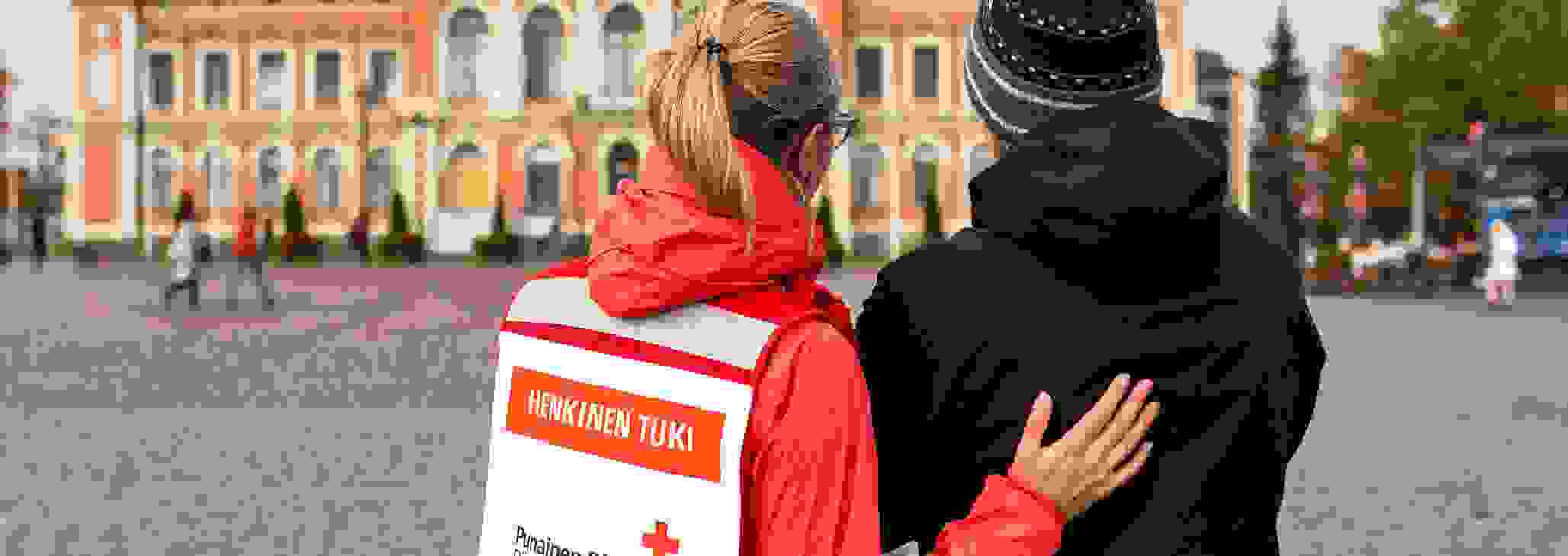 Henkilö Punaisen Ristin vapaaehtoisliiveissä keskustelee järkyttyneen miehen kanssa Kuopion torilla.