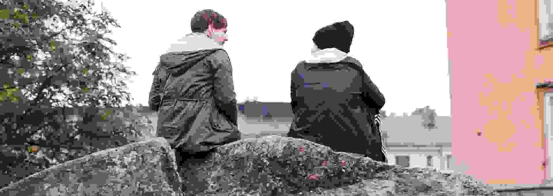 Kaksi nuorta aikuista keskustelee syksyisessä maisemassa kalliolla istuen.