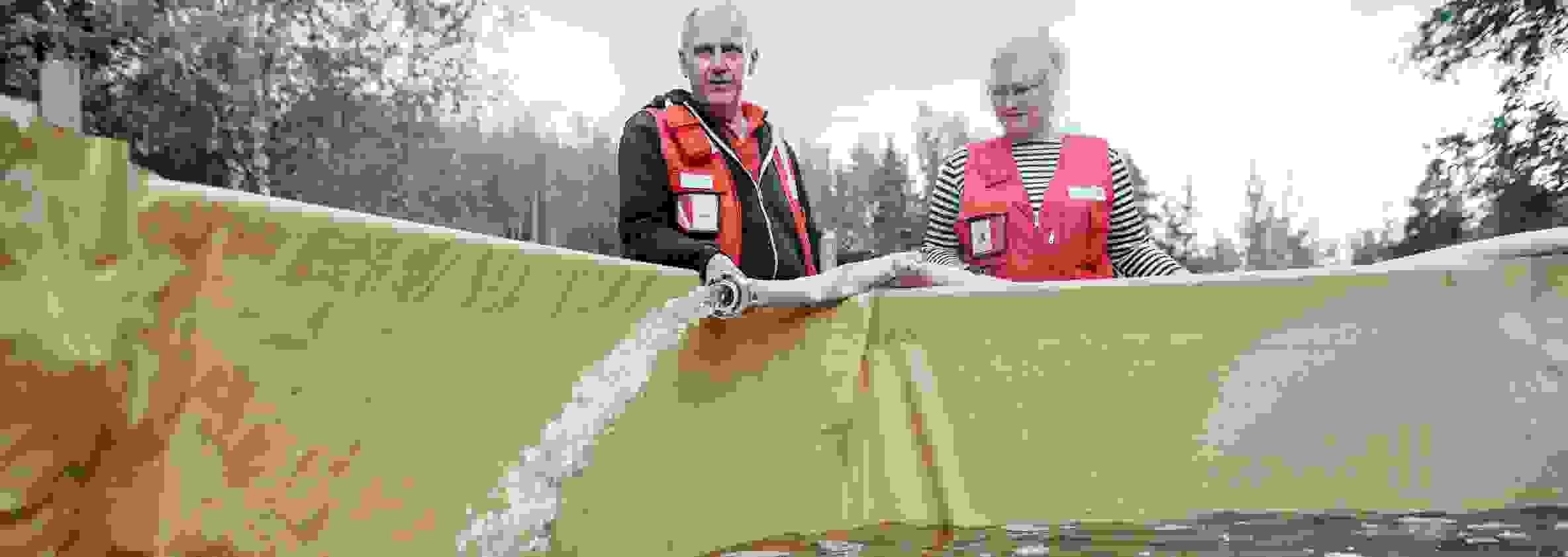 Kaksi henkilöä Punaisen Ristin varusteissa täyttää vesiallasta puhtaalla vedellä.