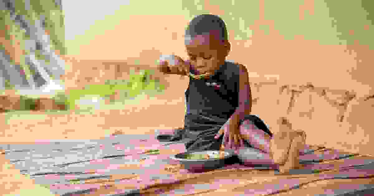 Pieni lapsi istuu maassa syömässä.
