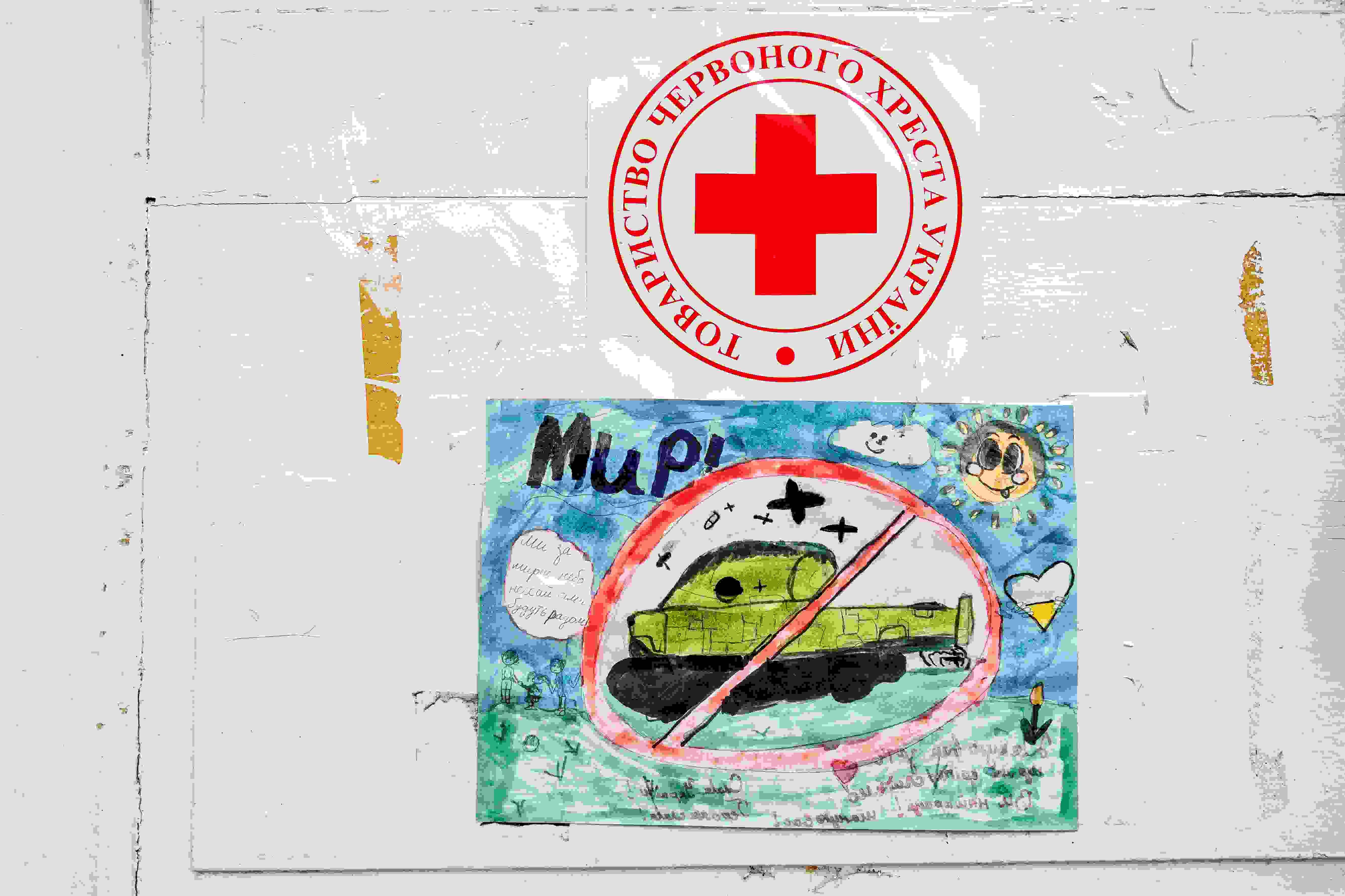 Lapsen piirros panssarivaunusta, yläpuolella Punaisen Ristin logo.