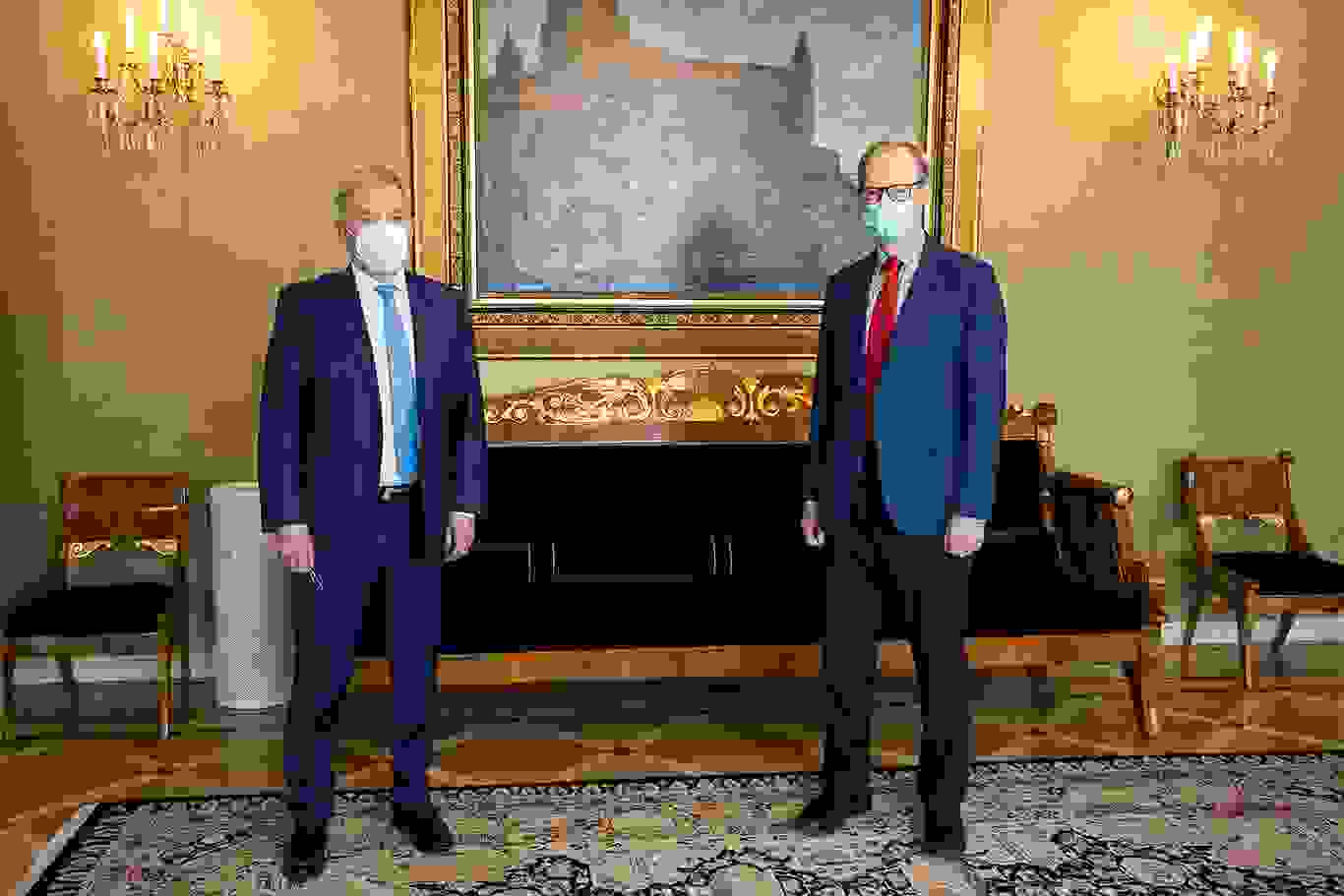Sauli Niinistö ja Pertti Torstila kasvoillaan maskit seisovat taululla ja kristallikruunuilla sisustetussa huoneessa.