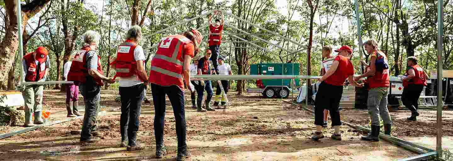 Kolmetoista Punaisen Ristin avustustyöntekijää rakentaa sairaalatelttaa aurinkoisella aukiolla Bangladeshissa.