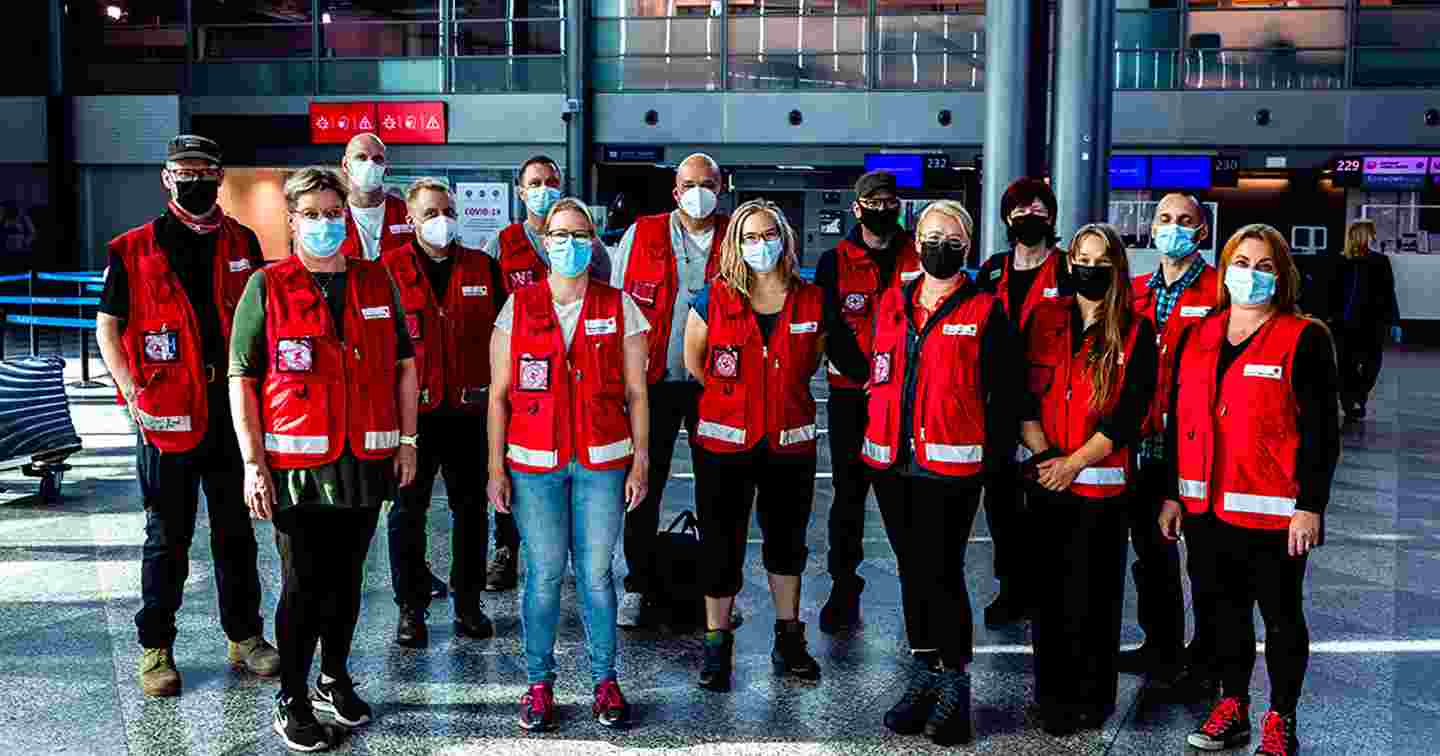 Neljätoista avustustyöntekijää Punaisen Ristin asuissa maskit kasvoillaan Helsinki-Vantaan lentoasemalla.