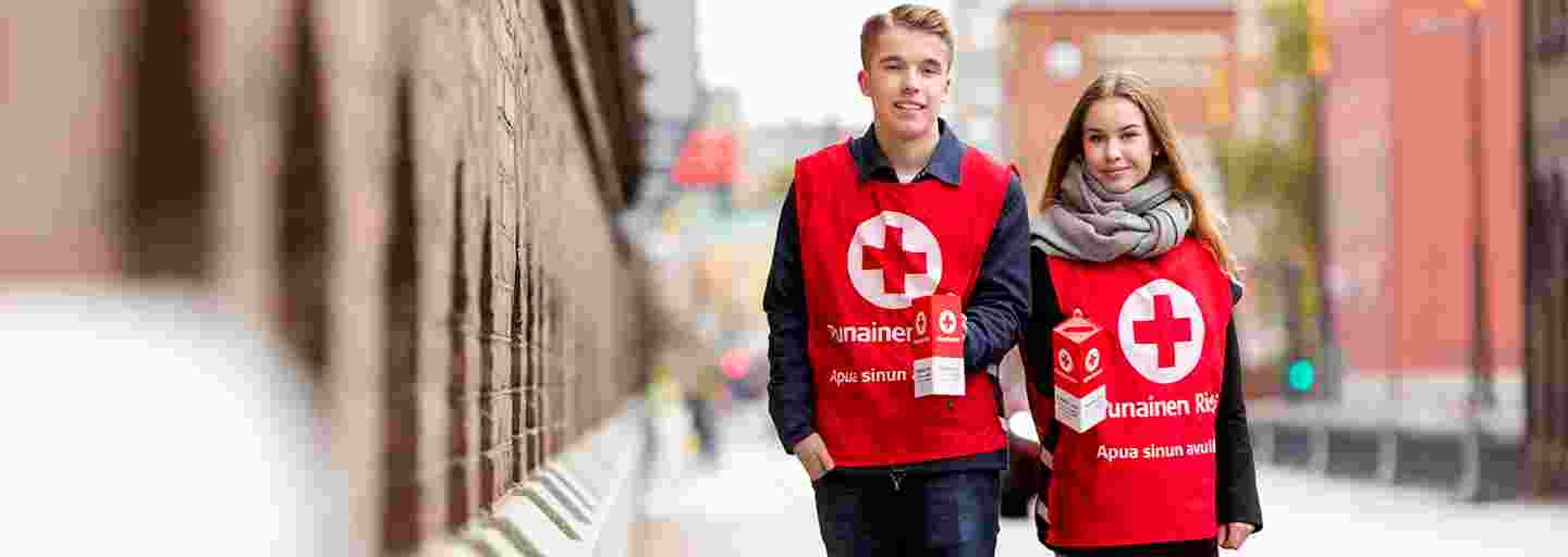 Kaksi nuorta lipaskerääjää hymyilevät käsissään keräyslippaat ja yllään Punaisen Ristin keräysliivit.