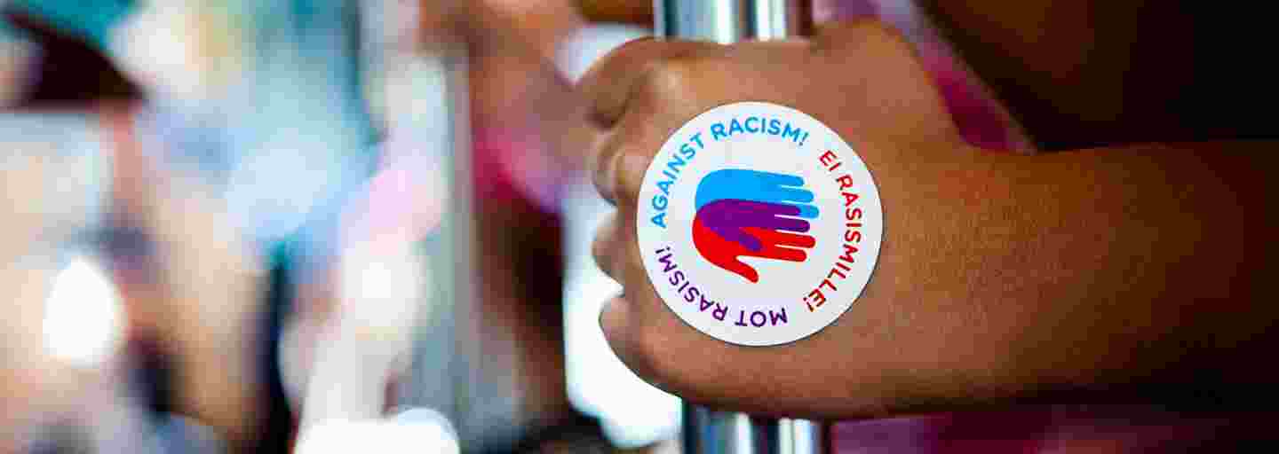 Raitiovaunussa tangosta kiinni pitävä käsi, jossa on Ei rasismille -logotarra.