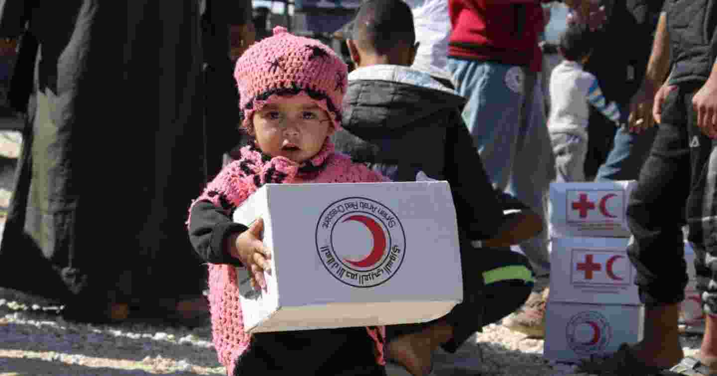 Pieni syyrialainen lapsi Punaisen Ristin avustuspaketti kädessään