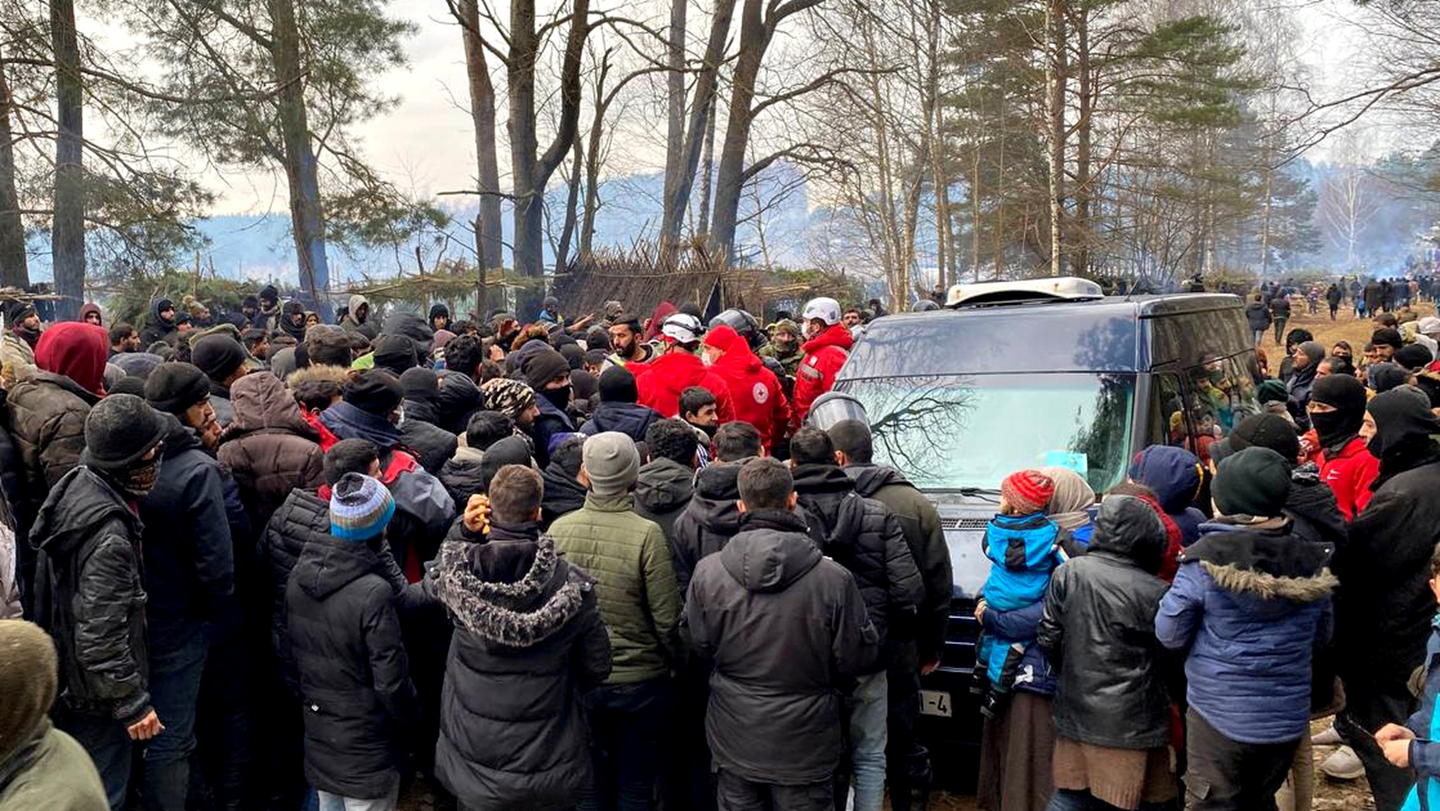 Valko-Venäjän Punaisen Ristin avustustyöntekijät seisovat suuren ihmisjoukon keskellä. 