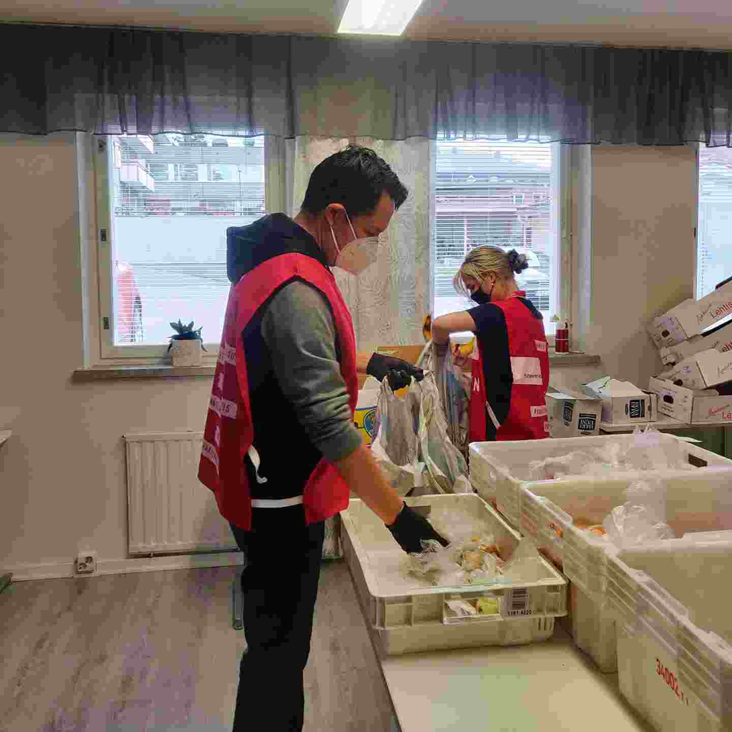 Punaisen Ristin vapaaehtoisliiveihin pukeutunut henkilö pakkaa ruokatarvikkeita pöydän ääressä.