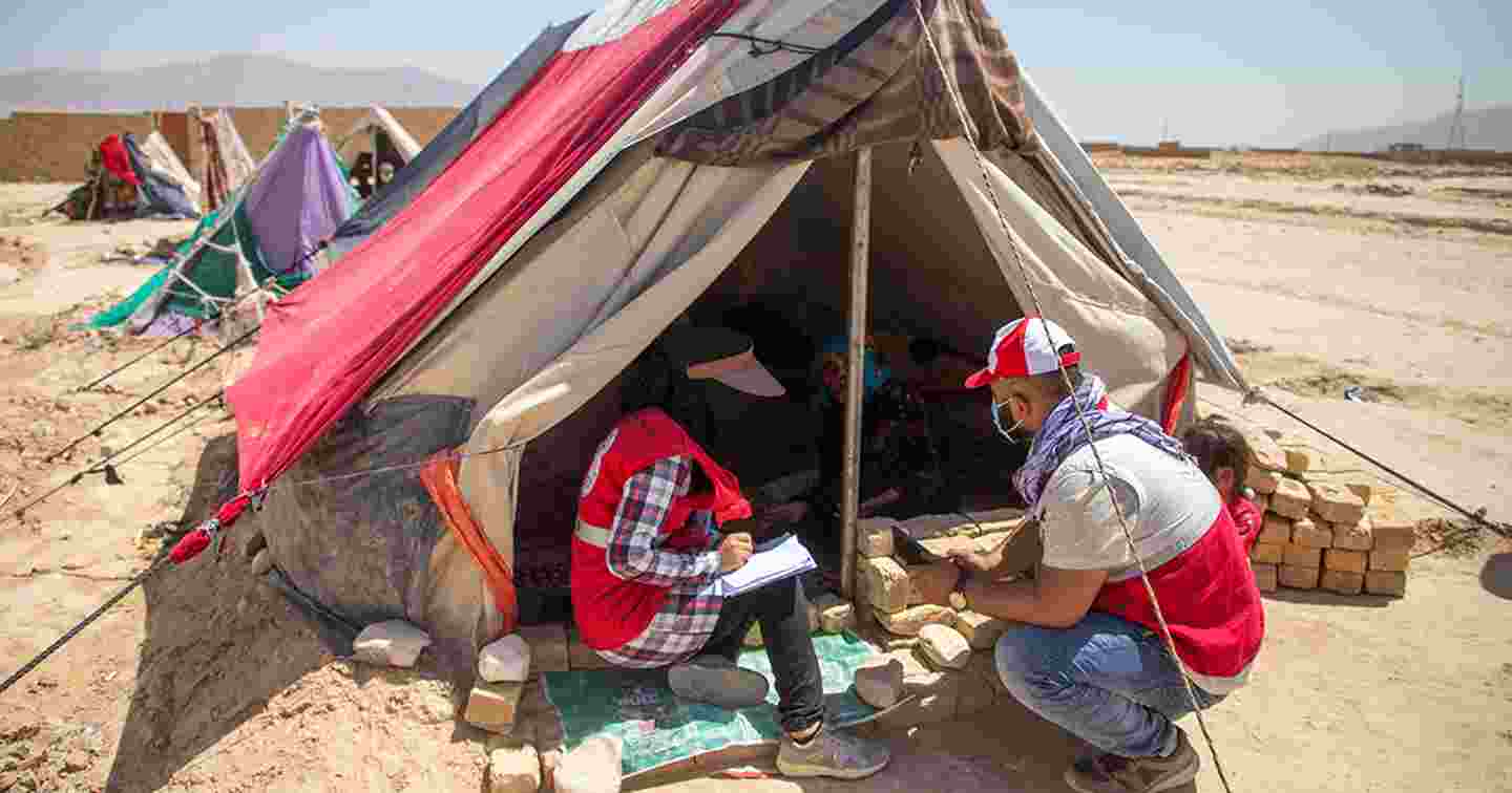 Kaksi Afganistanin Punaisen Puolikuun avustustyöntekijää keskustelee perheen kanssa teltan edessä.