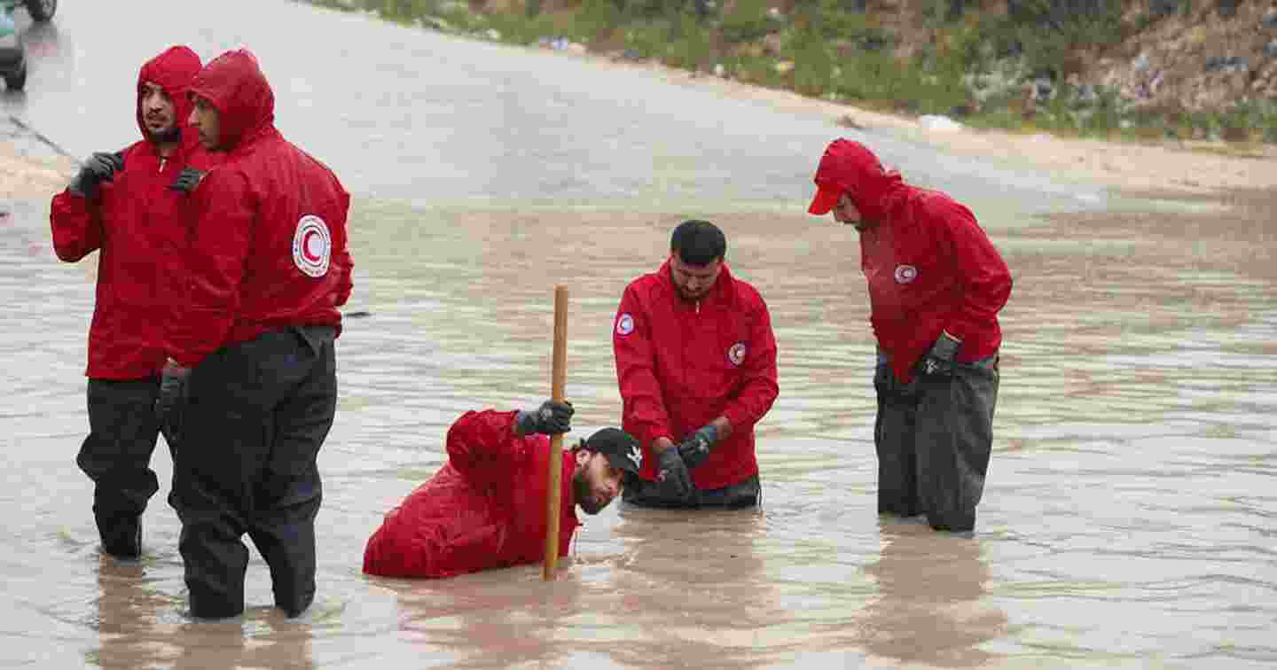 Henkilöt Punaisen Puolikuun liiveissä seisovat tulvaveden keskellä.