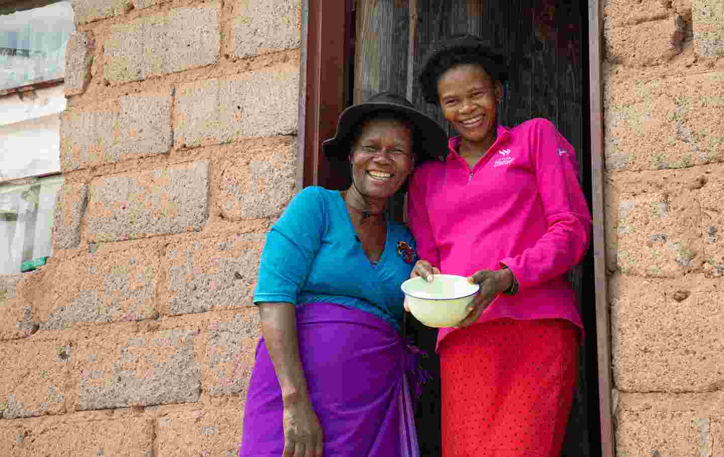 Kaksi hymyilevää ihmistä kotitalonsa edessä Eswatinissa.