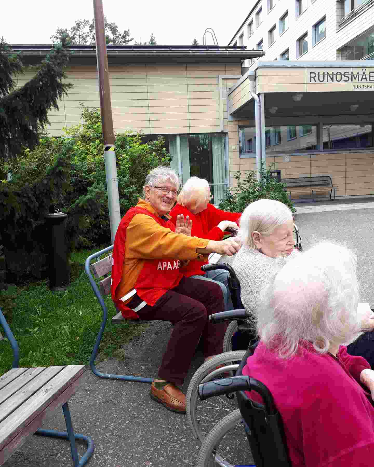 Hymyilevä Punaisen Ristin vapaaehtoinen ulkoiluttaa iäkkäitä palvelutalon asukkaita.