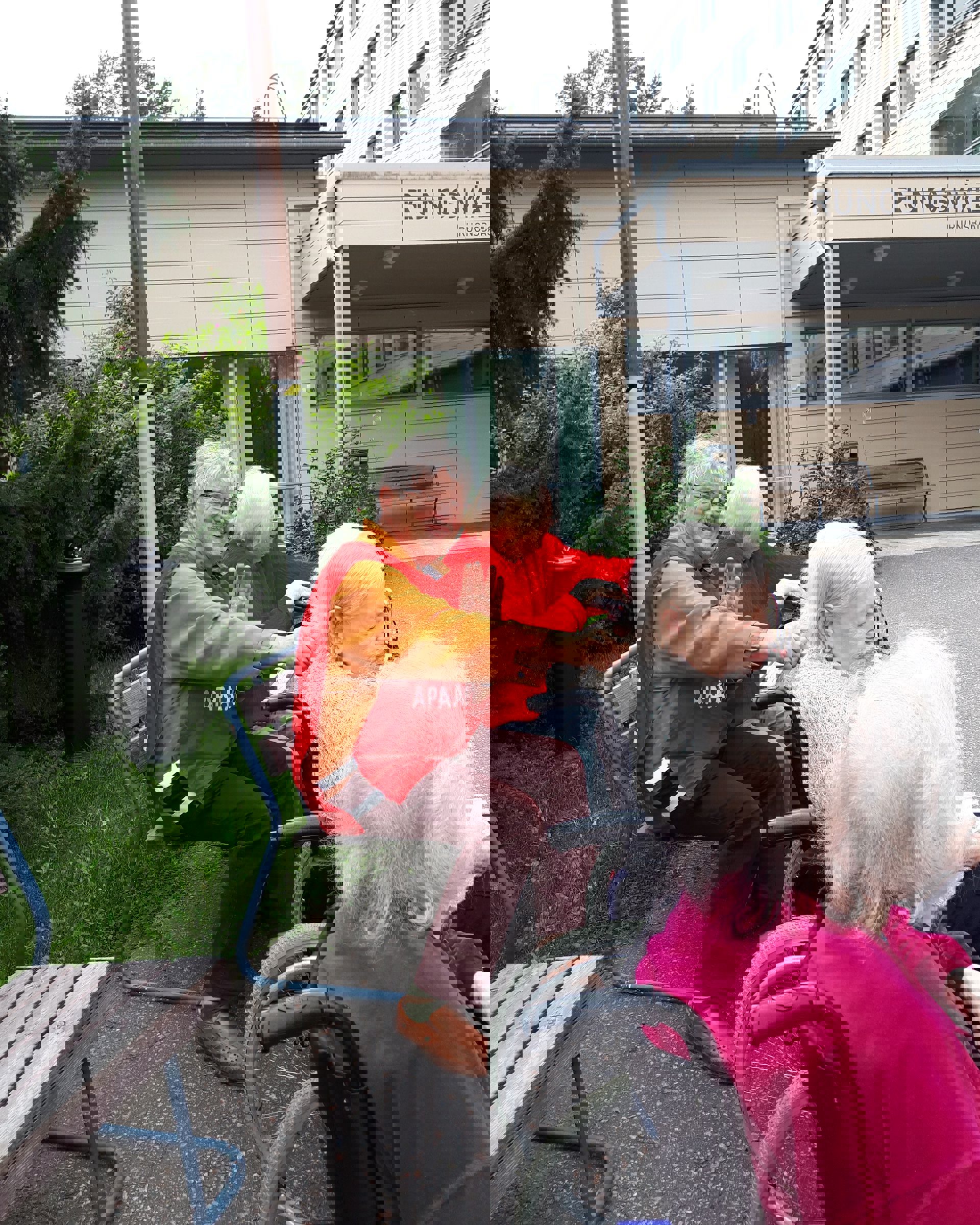 Hymyilevä Punaisen Ristin vapaaehtoinen ulkoiluttaa iäkkäitä palvelutalon asukkaita.