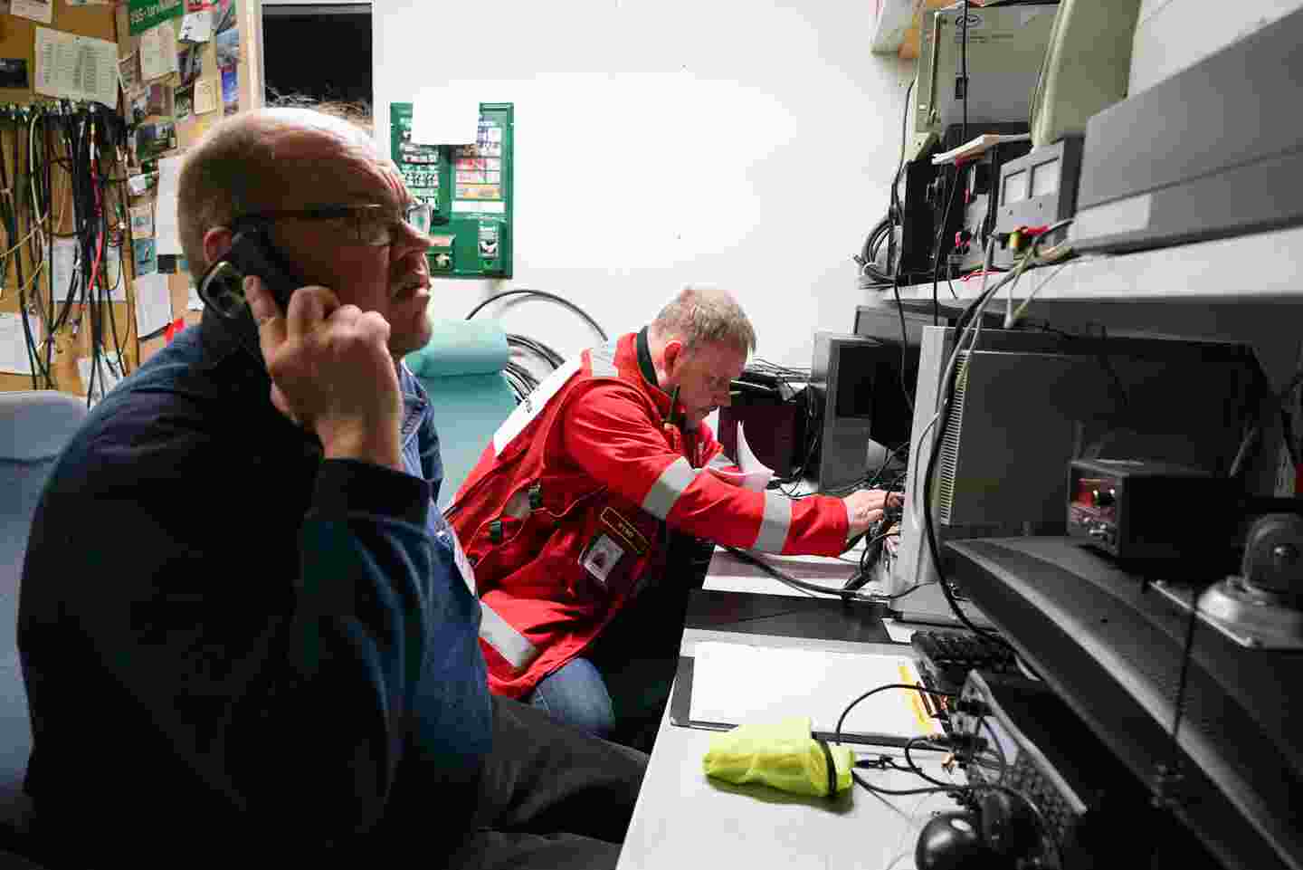 Punaisen Ristin ja Vapaaehtoisen pelastuspalvelun vapaaehtoiset teknisessä tilassa laitteiden keskellä. Toinen vapaaehtoisista puhuu puhelimeen.
