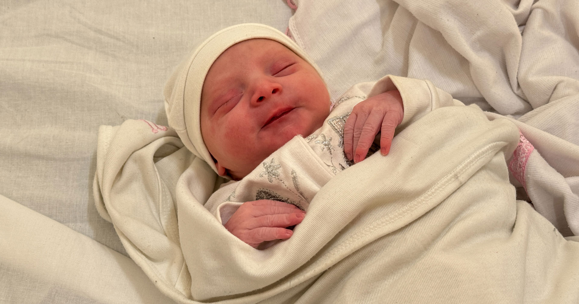 Vastasyntynyt vauva makaa silmät kiinni valkoinen pipo päässään ja tyytyväinen ilme kasvoillaan.