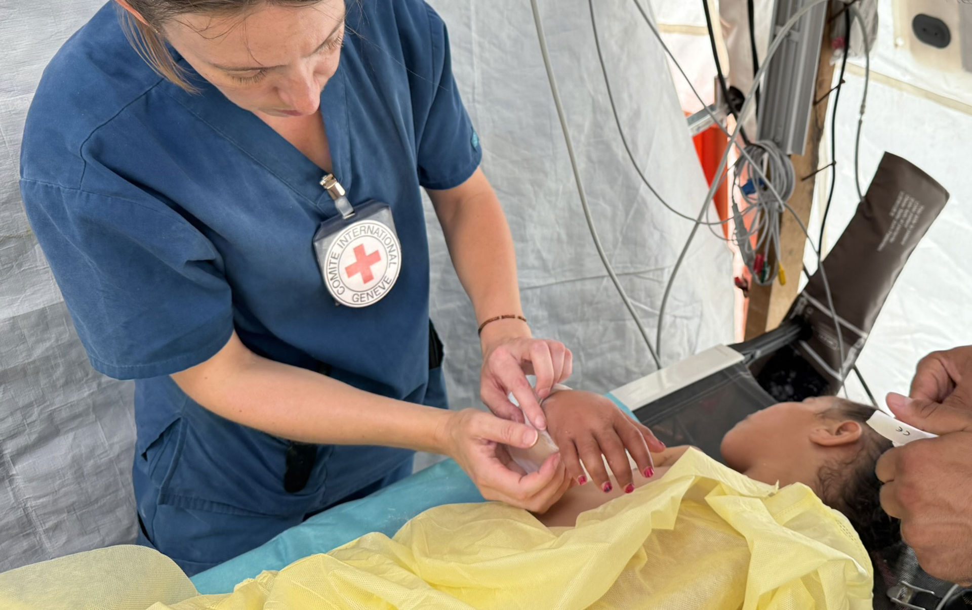 Punaisen Ristin fysioterapeutti laittaa kipsiä lapsipotilaan käsivarteen kenttäsairaalassa. Potilas makaa sängyssä keltainen lakana päällään.