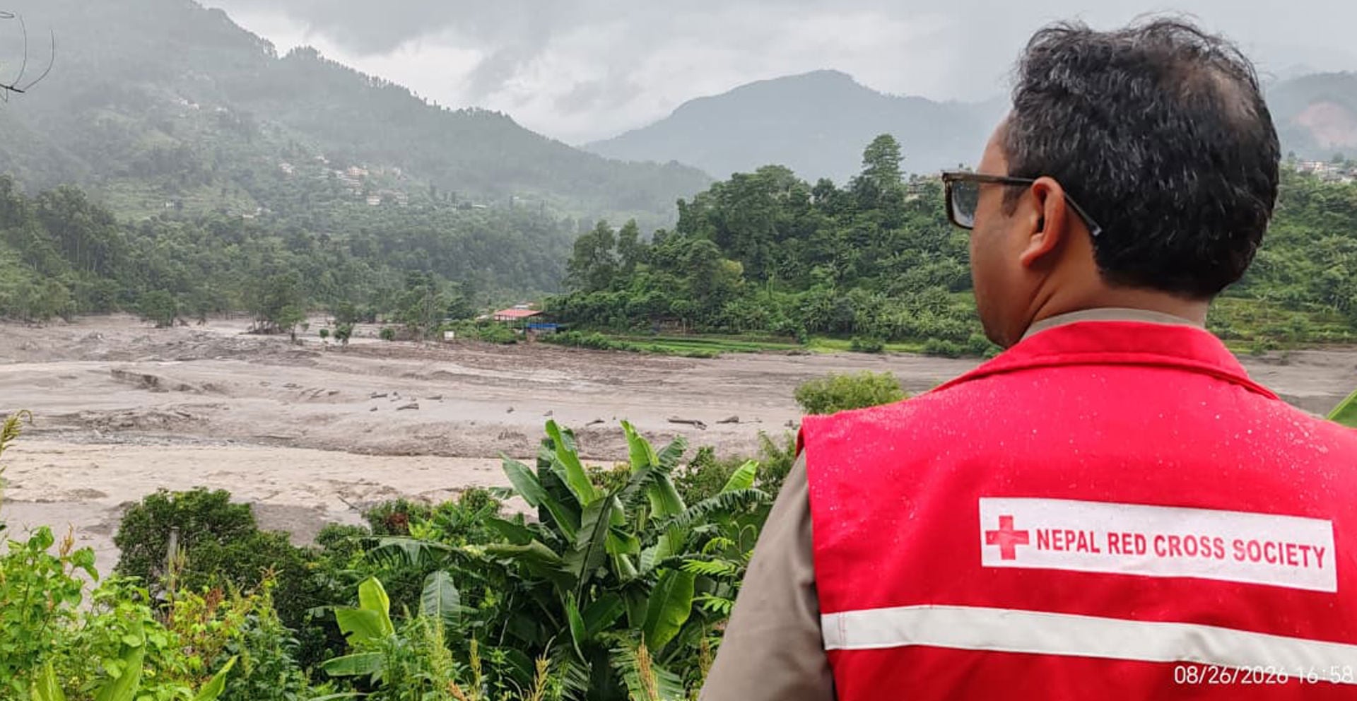 Nepalin Punaisen Ristin työntekijä katsoo tulvavahinkoja. Taustalla tulviva joki.