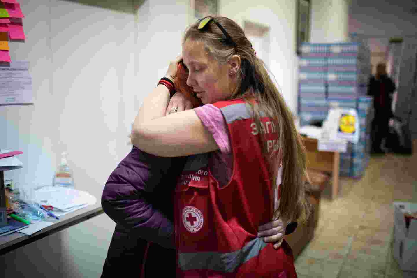 Henkilö Punaisen Ristin vaatteissa halaa toista henkilöä.