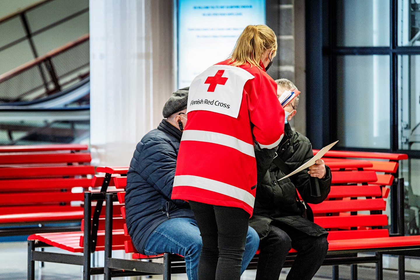 Punaisen Ristin vaatteisiin pukeutunut vapaaehtoinen keskustelee pakolaisten kanssa satamassa.