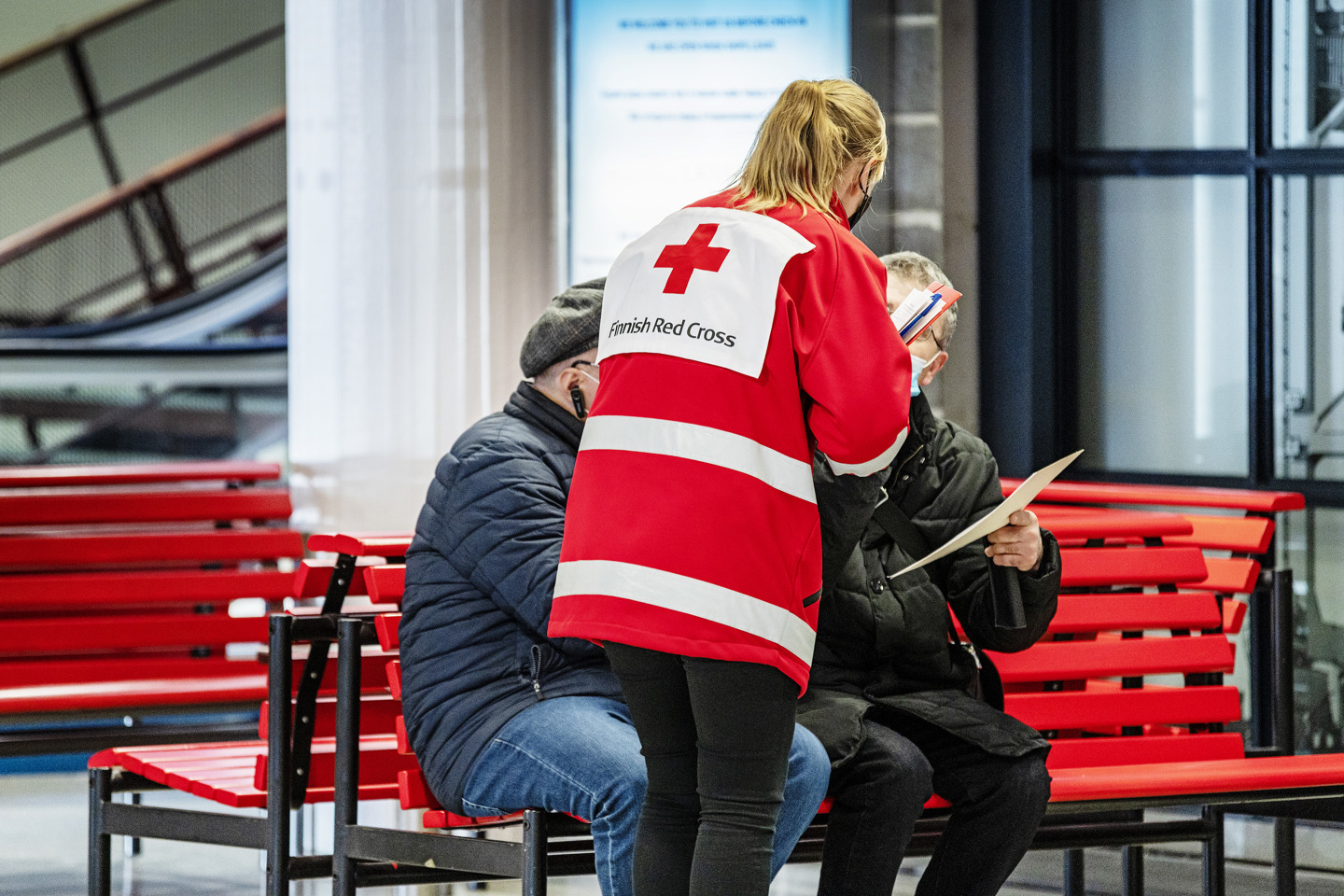 Punaisen Ristin vaatteisiin pukeutunut vapaaehtoinen keskustelee pakolaisten kanssa satamassa.