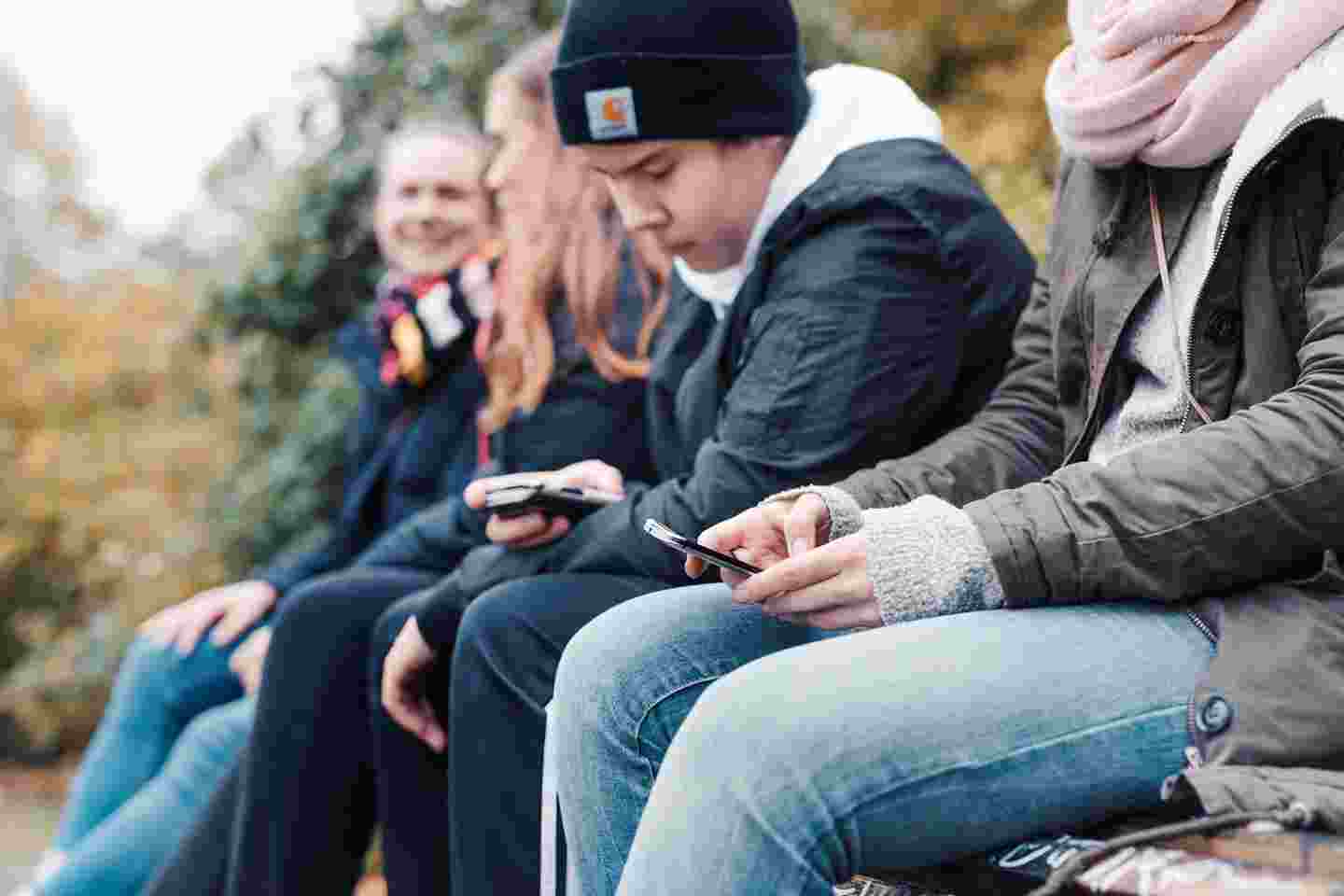 Neljä nuorta viettävät aikaa ulkona istuen. Kaksi heistä keskustelee, kaksi katsoo älypuhelimiaan.