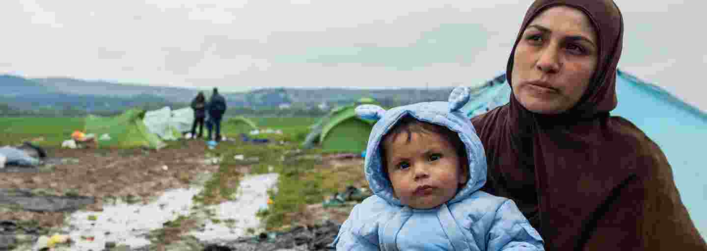 Äiti pitää lämpimästi puettua vauvaa sylissä pakolaisleirillä.