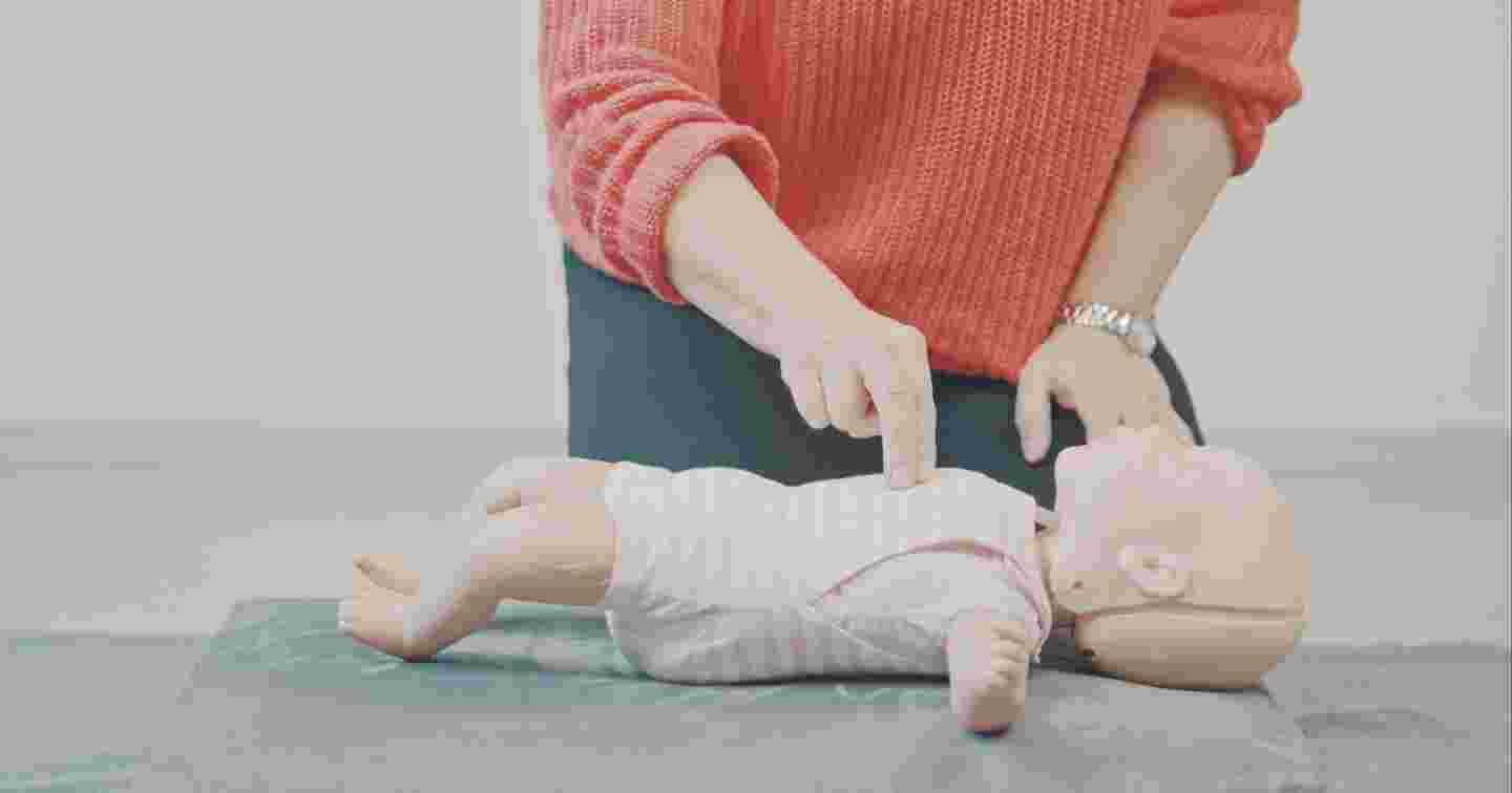 Henkilö harjoittelee vauvan paineluelvytystä lattialla elvytysnuken avulla.
