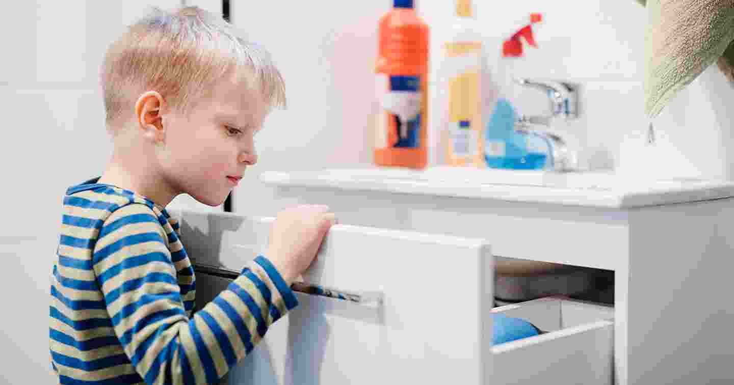 Lapsi kurkistaa kaappiin kylpyhuoneessa, jossa on erilaisia pesuaineita ja muita kemiallisia tuotteita.