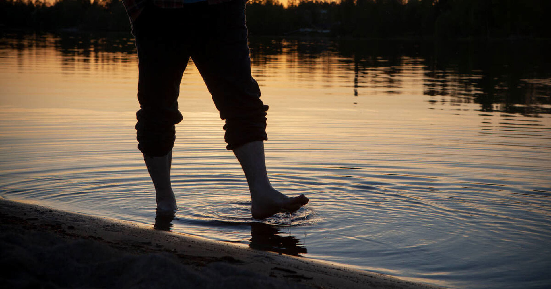 Henkilö seisoo rannalla kesäillassa.