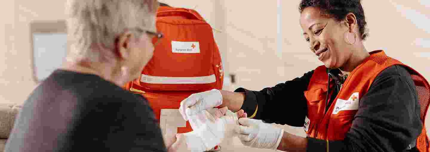 Punaisen Risti vapaaehtoinen sitoo toisen henkilön kädessä olevaa haavaa.