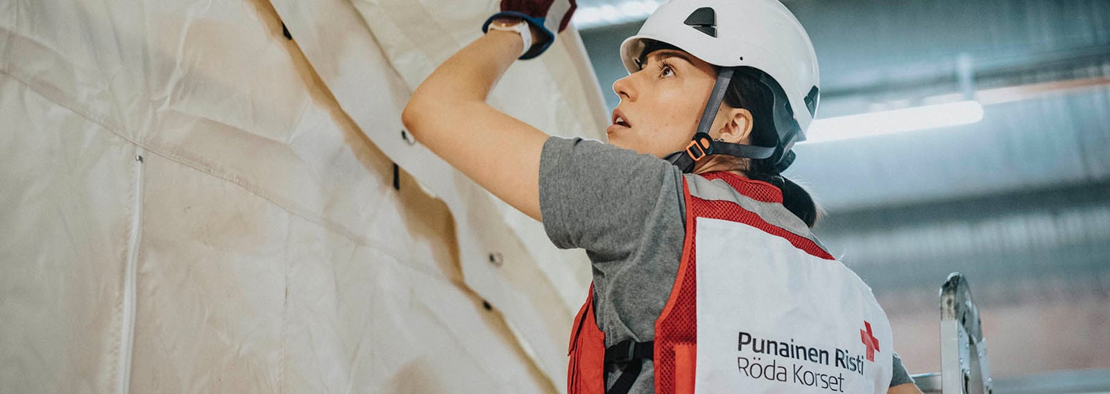 Punaisen Ristin vapaaehtoinen järjestön varusteissa työskentelee sairaalateltan pystytyksessä.