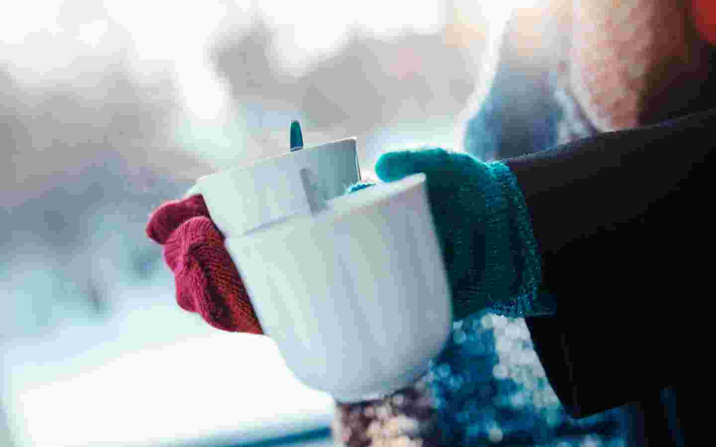 Kädet pitelevät kahvikuppeja ulkona talvisessa säässä.