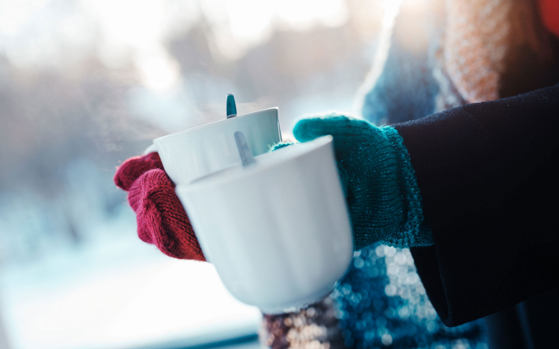 Kädet pitelevät kahvikuppeja ulkona talvisessa säässä.