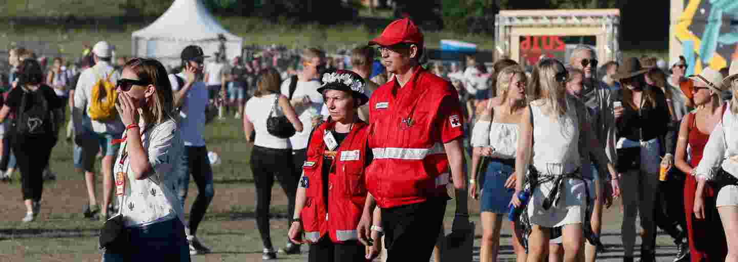 Mies ja nainen Punaisen Ristin vapaaehtoiliiveissä suorittavat päihdepäivystystä aurinkoisilla festivaaleilla.