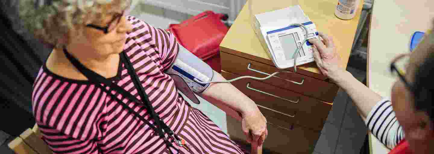 Henkilö Punaisen Ristin vapaaehtoisliiveissä mittaa verenpainetta iäkkäältä henkilöltä.