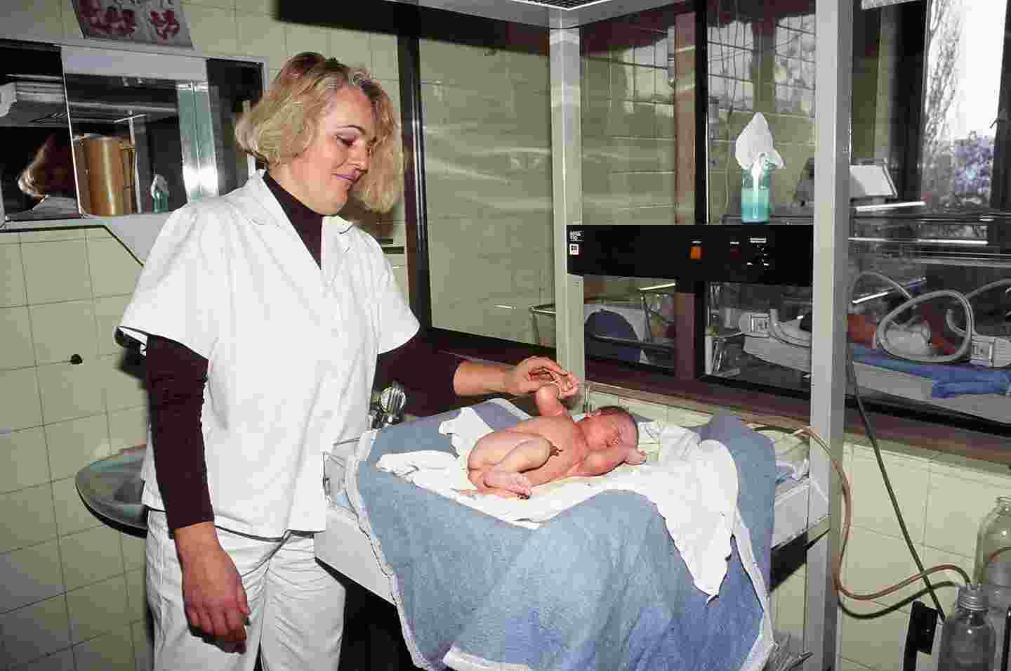 Sairaanhoitaja pitelee vastasyntynyttä kädessä sairaalan hoitotilassa.
