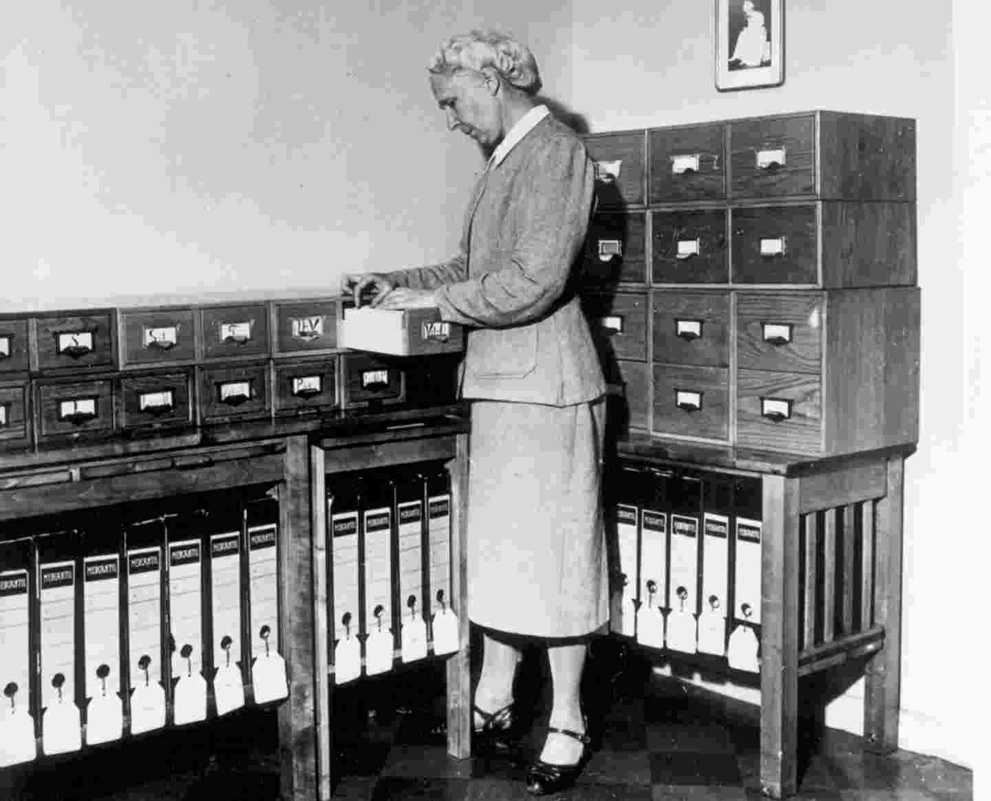 Iäkäs nainen lukee dokumenttia arkistokaappien edessä.