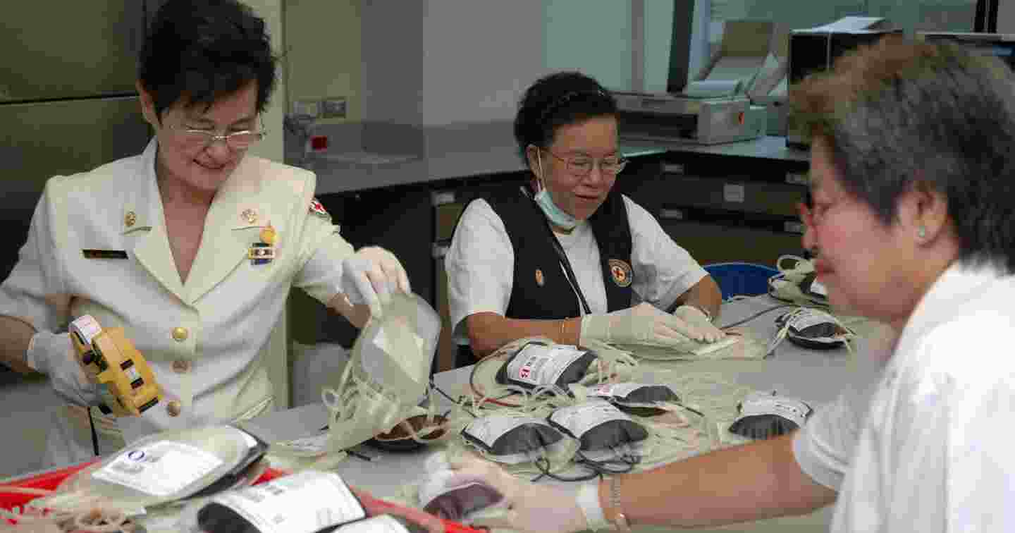 Kolme thaimaalaista naista työasuissa käsittelee veripusseja.