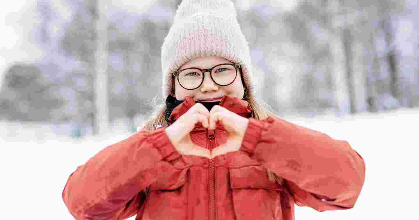 Talvisessa säässä hymyilevä nuori näyttää käsillään sydämen merkkiä.