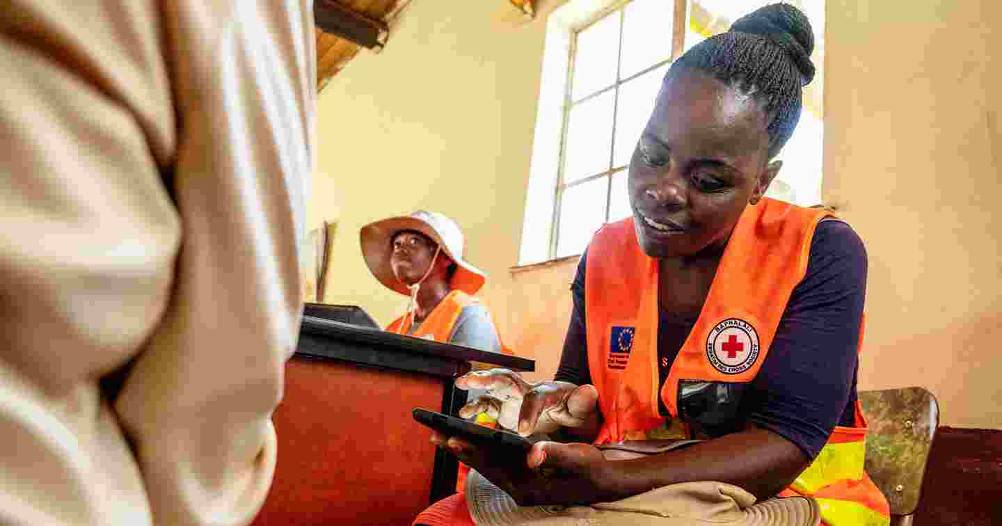 Punaisen Ristin avustustyöntekijä keskustelee henkilön kanssa käteisavustuspisteellä.