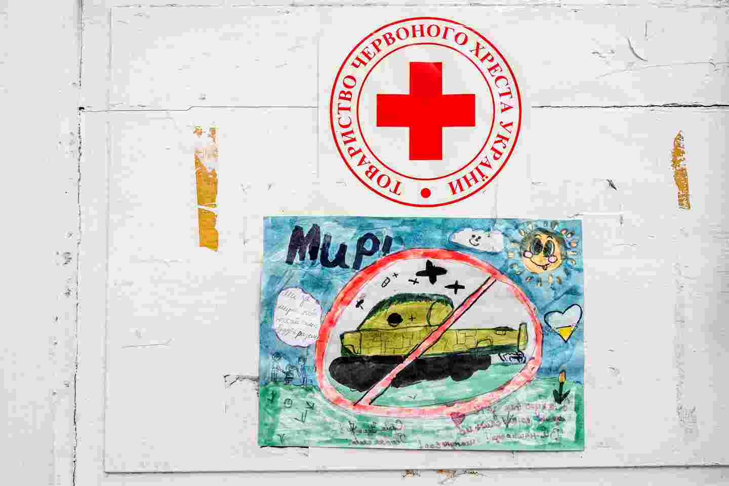 Lapsen piirros panssarivaunusta, yläpuolella Punaisen Ristin logo.