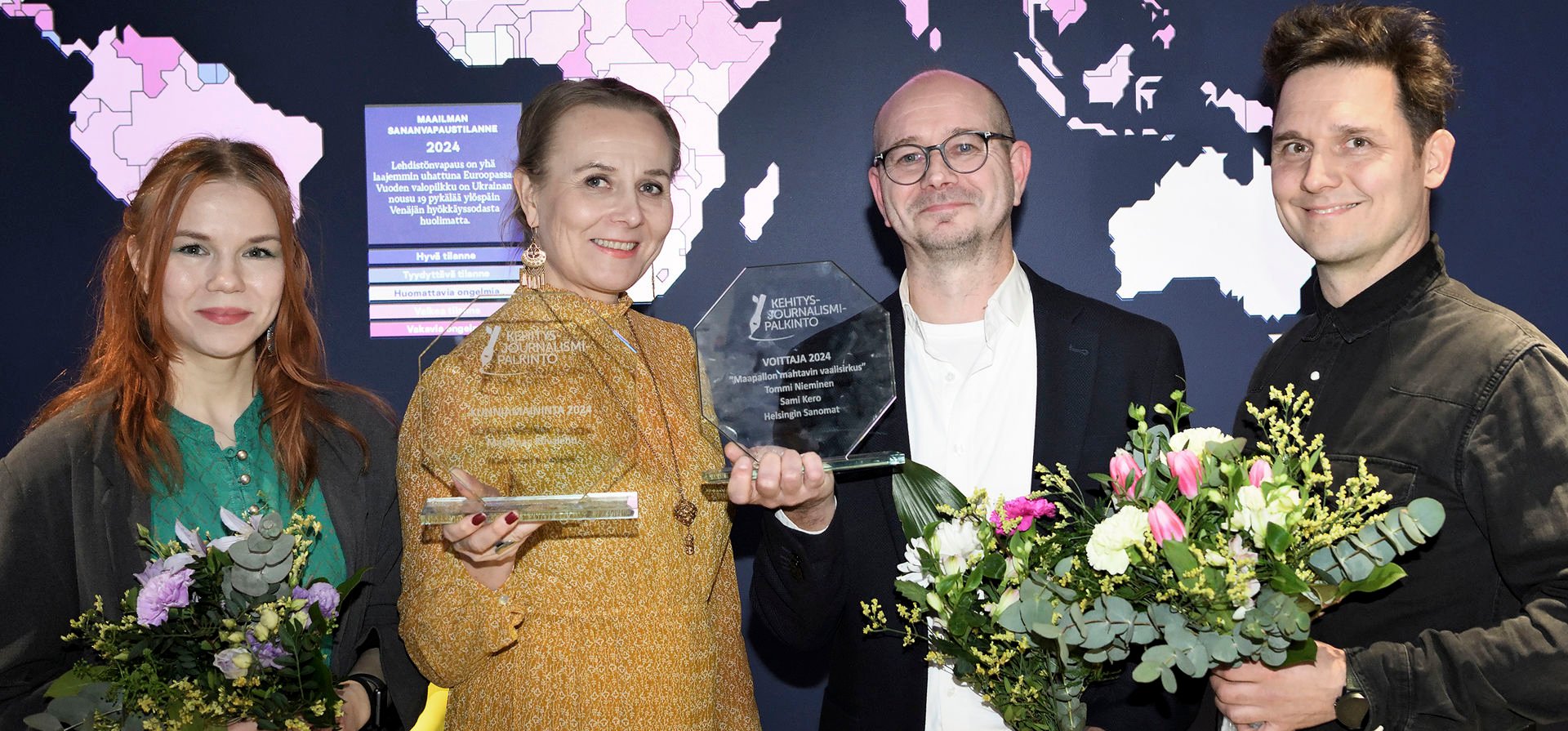 Viime vuoden palkitut seisovat rivissä palkintojen ja kukkakimppujen kanssa.