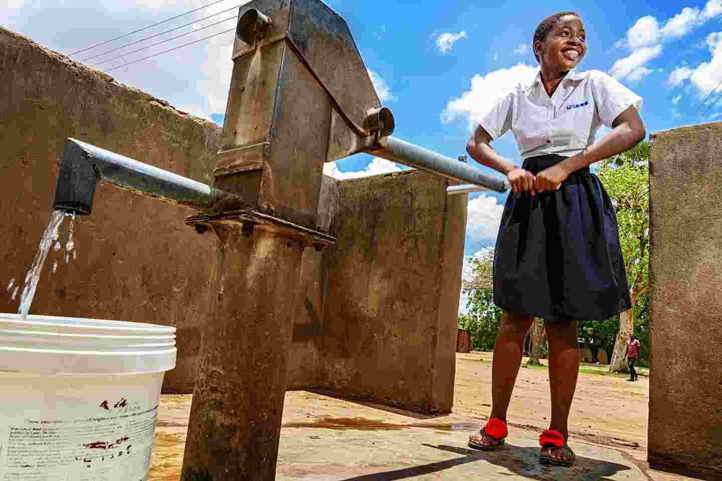 Hymyilevä nuori nainen pumppaa vettä kaivosta.
