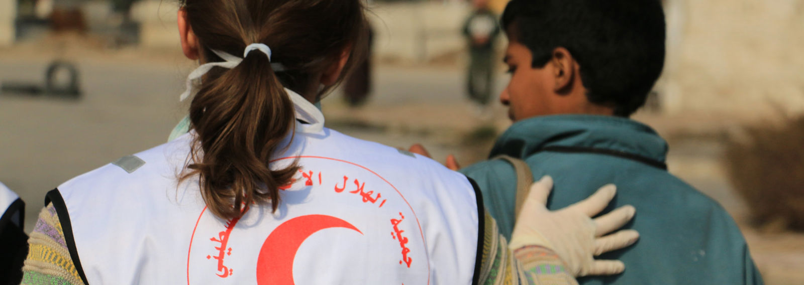 Punaisen Puolikuun liiviin sonnustautunut nainen avustaa nuorta miestä.