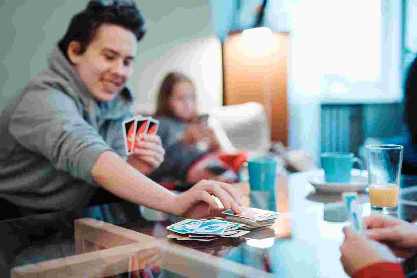 Hymyilevä nuori henkilö pelaa UNO-korttipeliä Nuorten turvatalossa muiden nuorten kanssa.