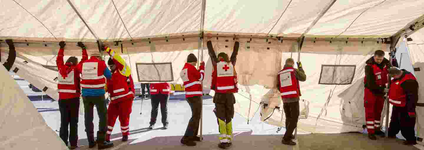 Seitsemän Punaisen Ristin varusteisiin sonnustautunutta ihmistä pystyttää telttaa.